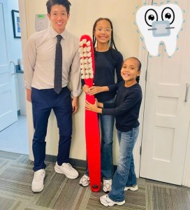 Group of three people holding a giant red tooth brush